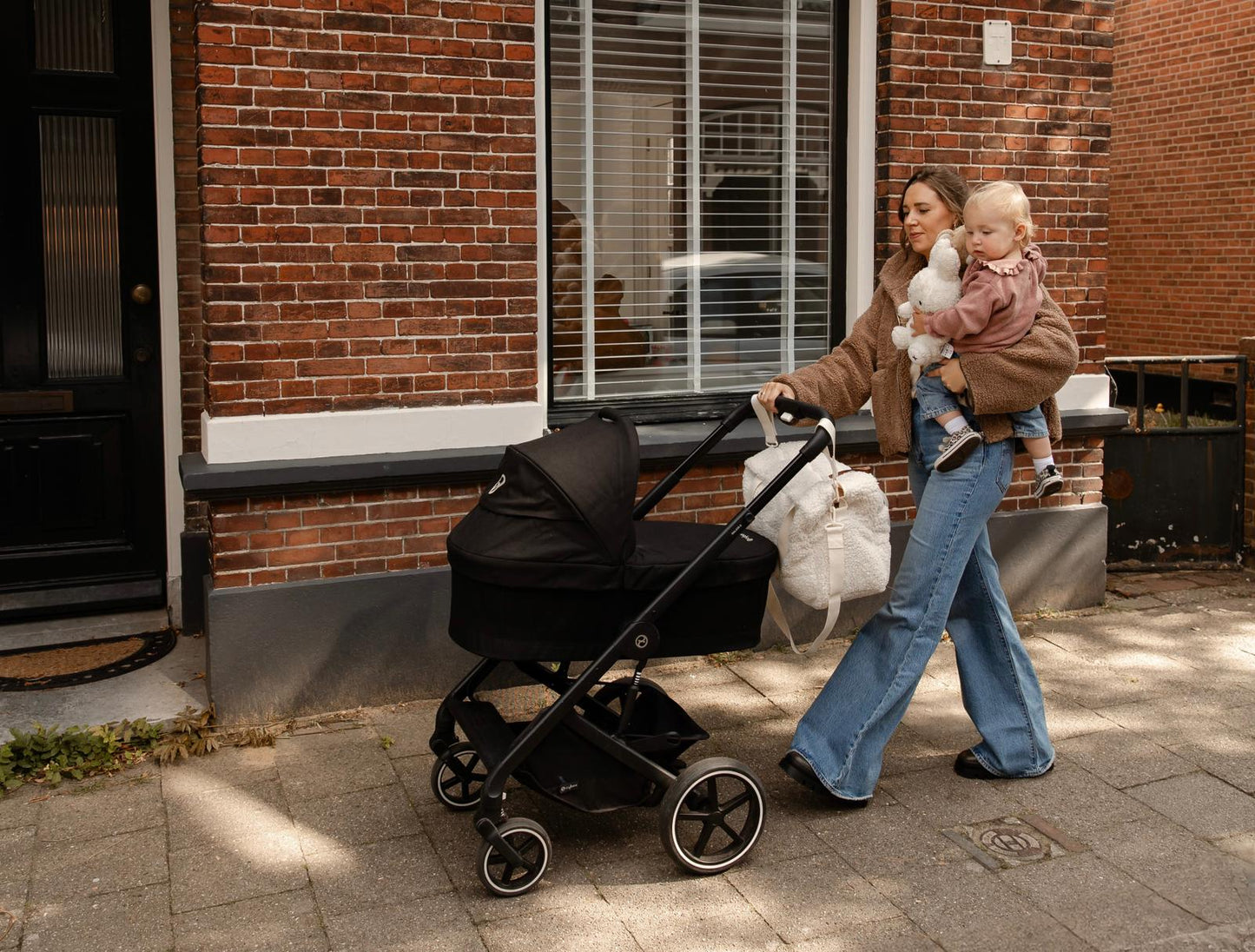 Moeder met kind op de arm met luiertas aan de kinderwagen met D-haken