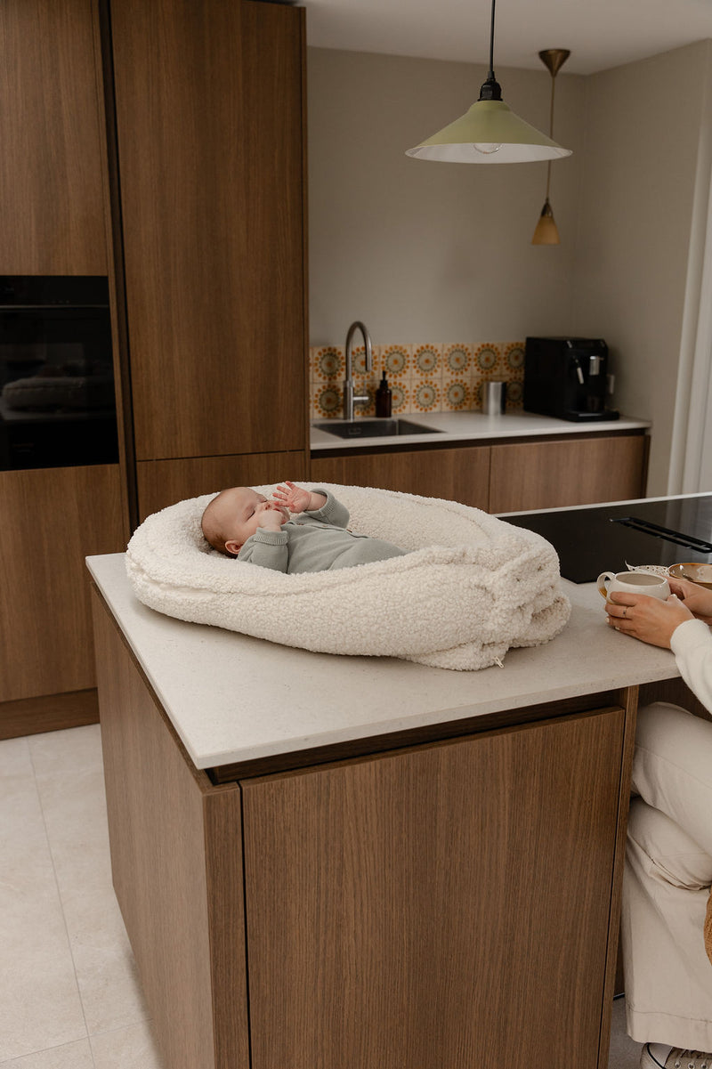 Baby ligt in het Benni & Ninni Teddy Babynest Cream op keukenblad

