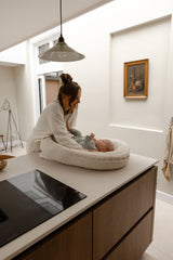Moeder plaatst baby in Benni & Ninni Teddy Babynest Cream op keukenblad

