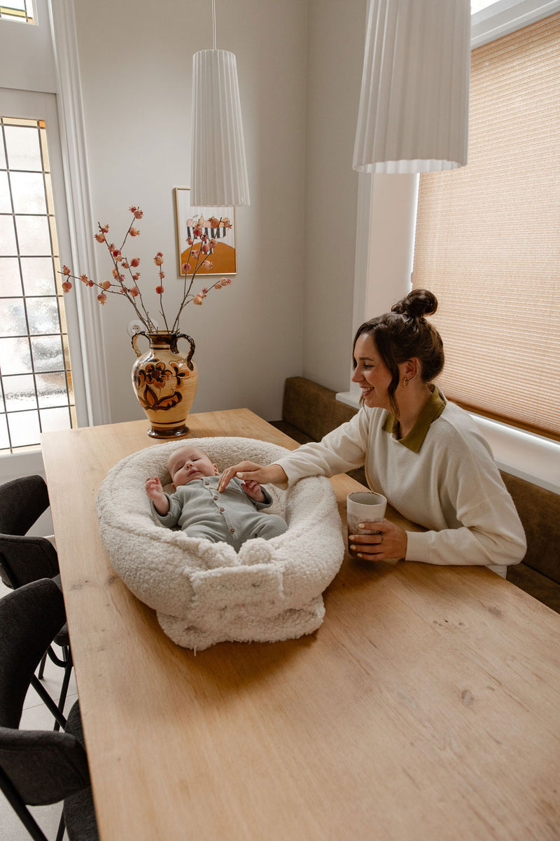 Moeder zit aan tafel met baby in het Benni & Ninni Teddy Babynest Cream


