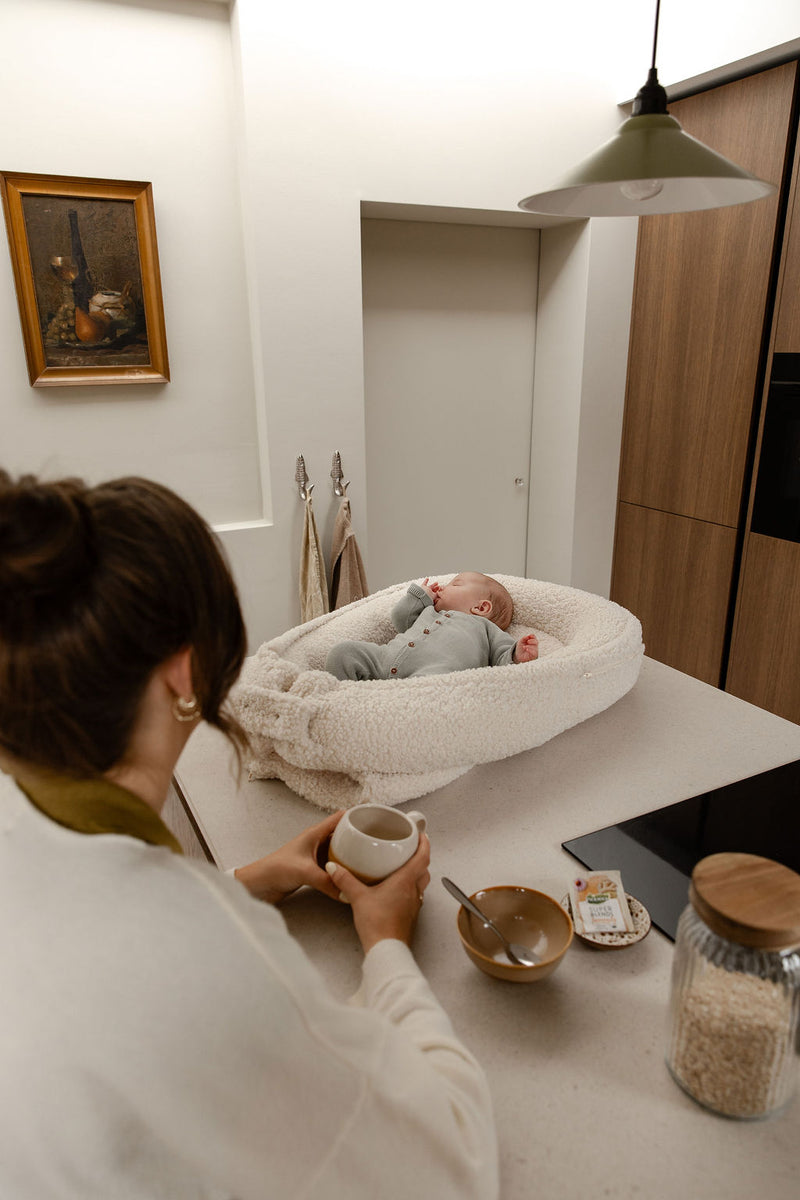 Moeder ontbijt naast baby in Benni & Ninni Teddy Babynest Cream op keukenblad