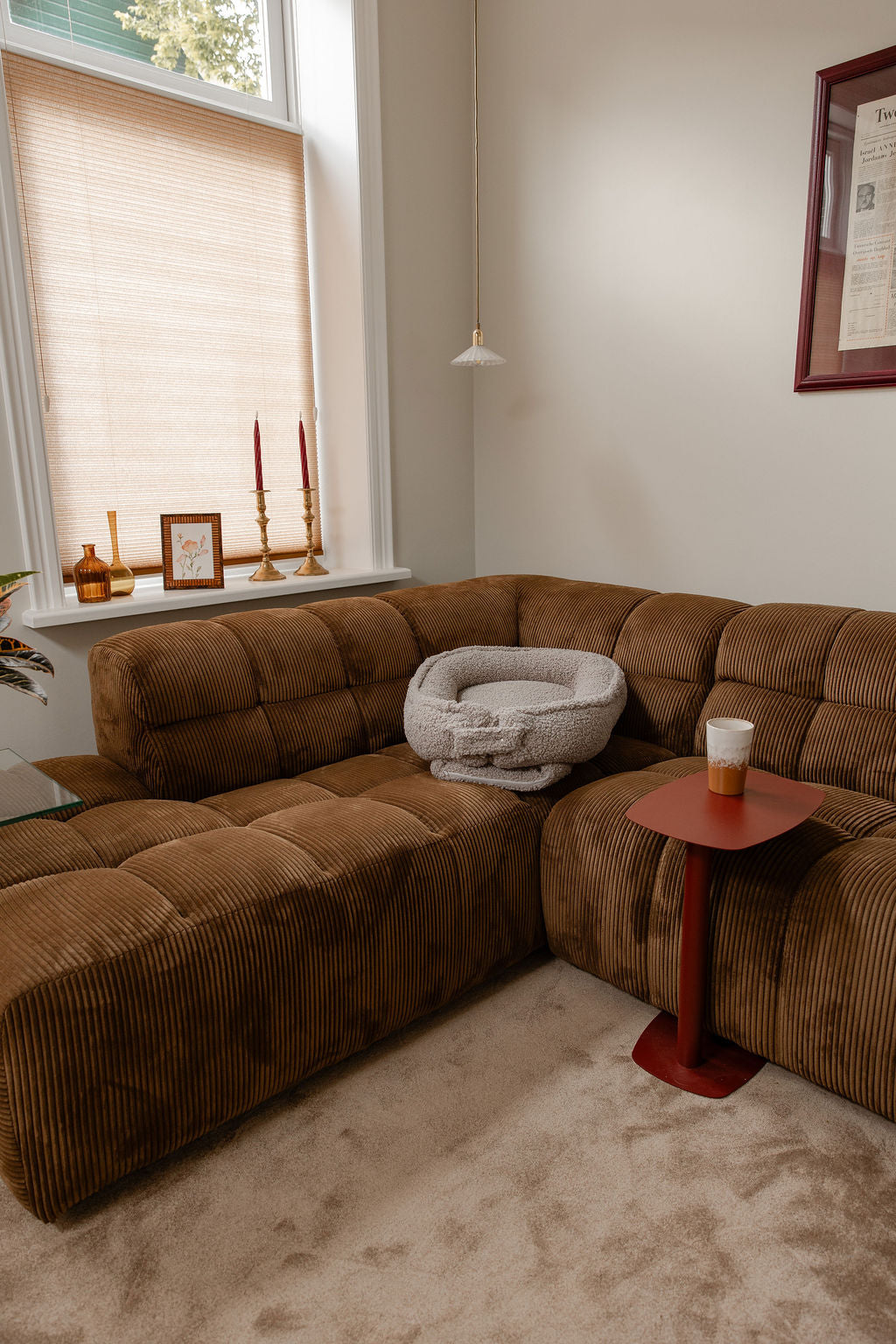 Het Benni & Ninni Teddy Babynest in de kleur Tan ligt stijlvol op een bank. Een warme, zachte plek voor je baby in de woonkamer, met stijlvol design dat past in elk interieur.