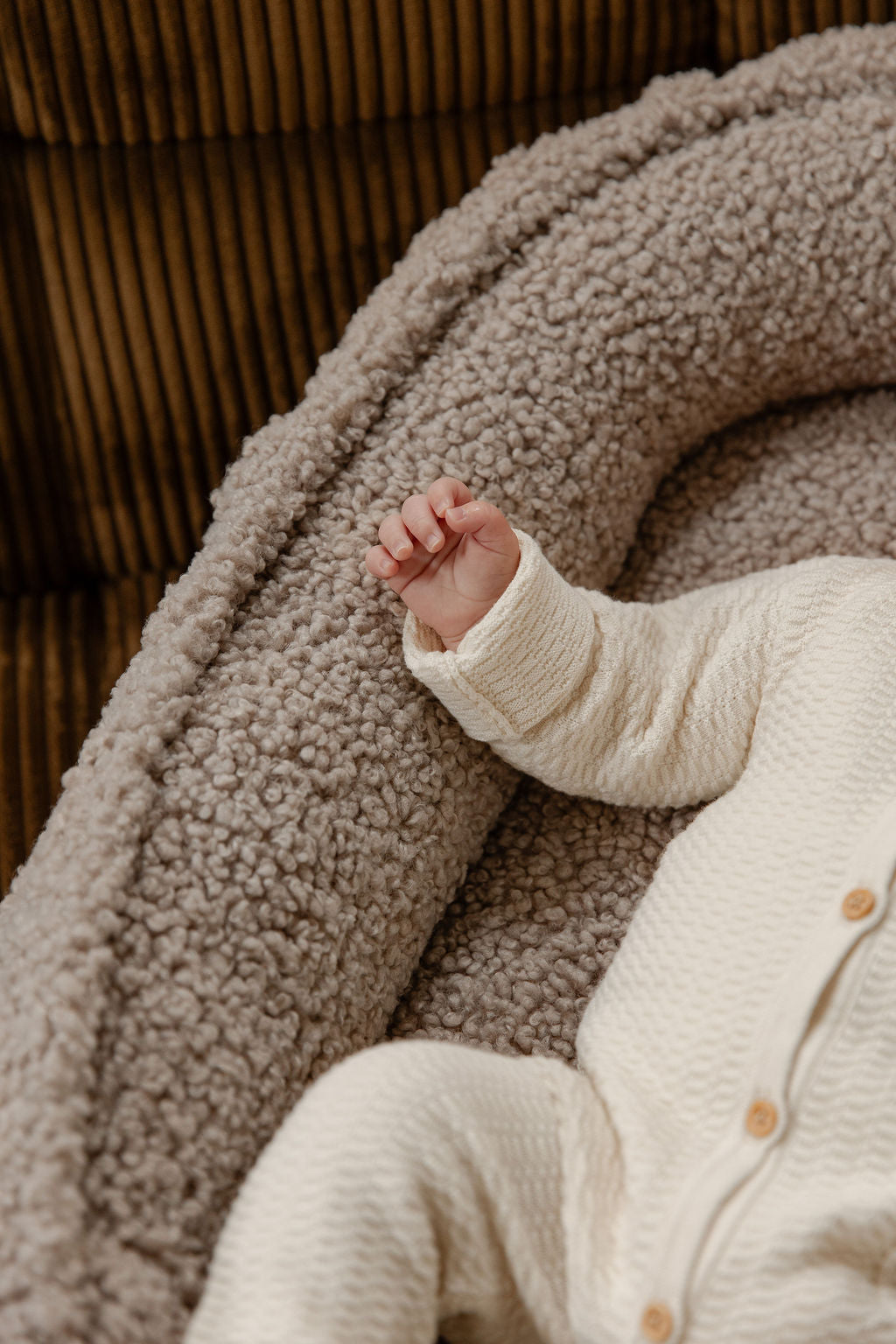 Close-up van de luxueuze teddystof van het Benni & Ninni Babynest Tan. De zachte textuur in combinatie met het schattige babyhandje straalt comfort en kwaliteit uit.

