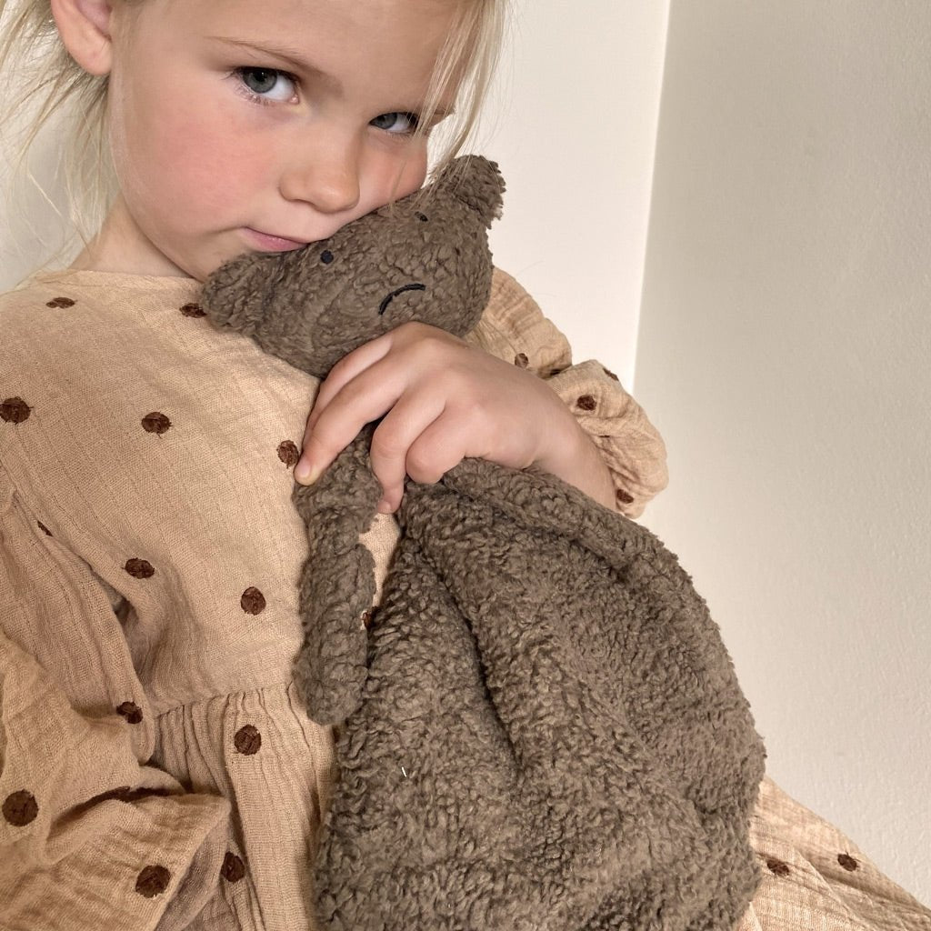 Baby die knuffelt met het Nuuroo Asta Knuffeldoekje Aap in een warme, rustgevende omgeving.