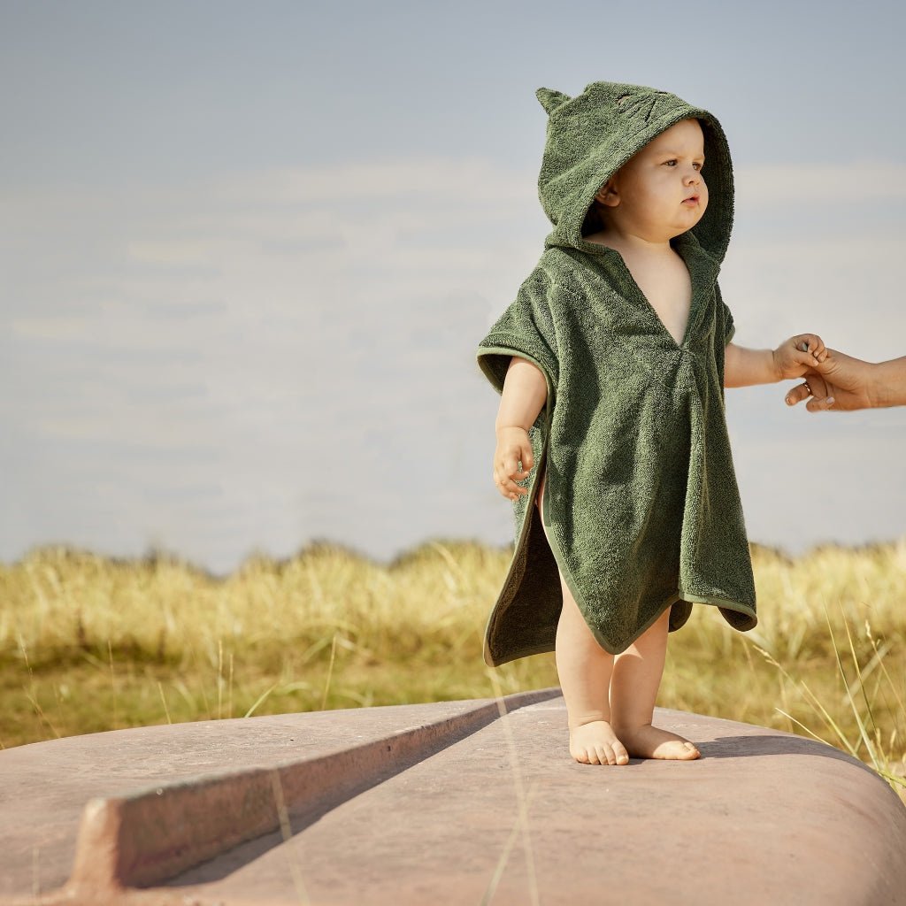 Kind draagt donkergroene badponcho met koala-oren op een zonnig strand


