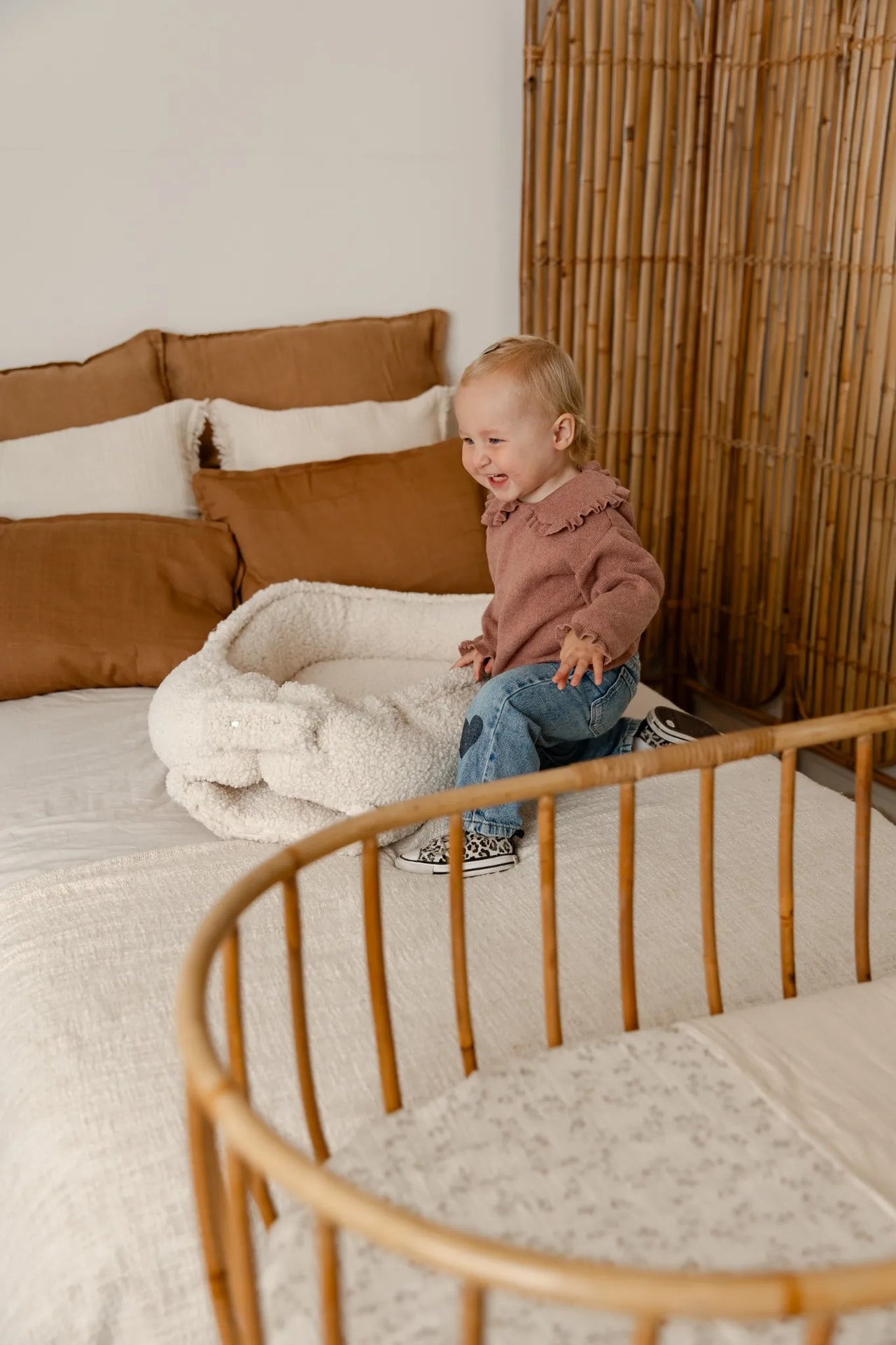 Blije baby naast een teddy babynestje in cream kleur op een bed.