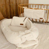 Babynestje teddy cream samen met luieretui en  crib organizer cream aan een wieg.
