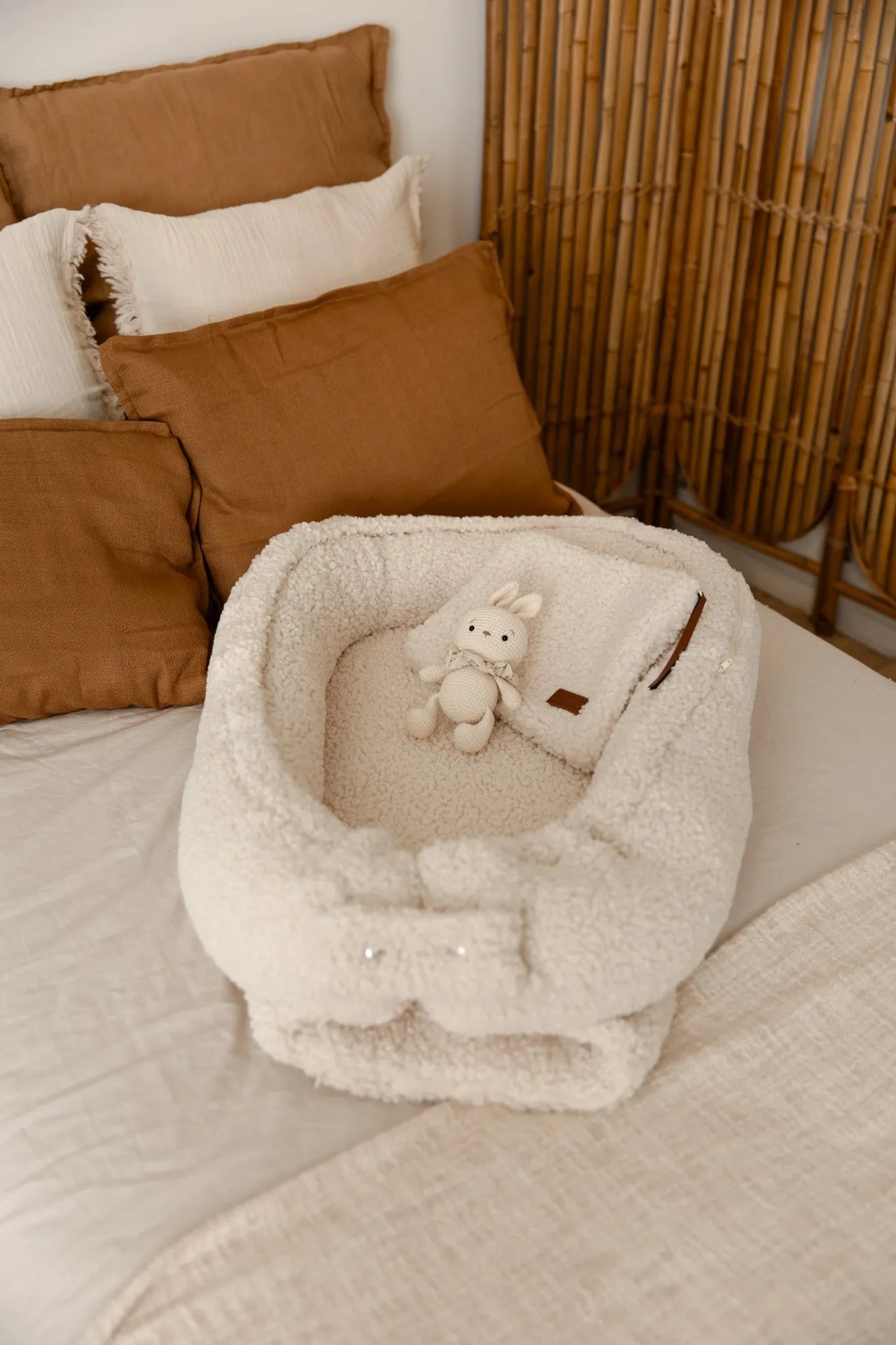 Teddy babynestje in cream kleur met knuffel erin op een bed.