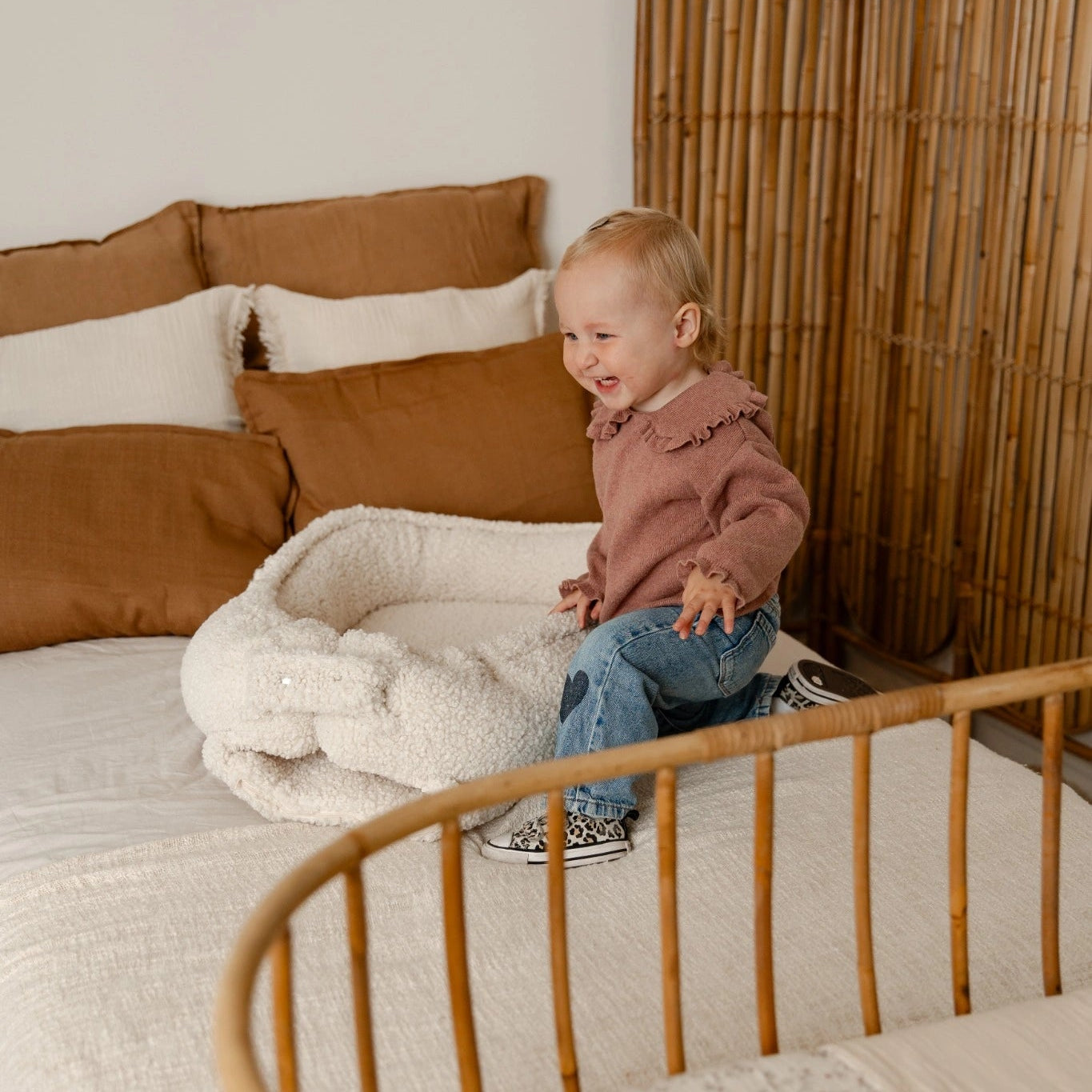 Peuter speelt naast teddy babynest cream op bed