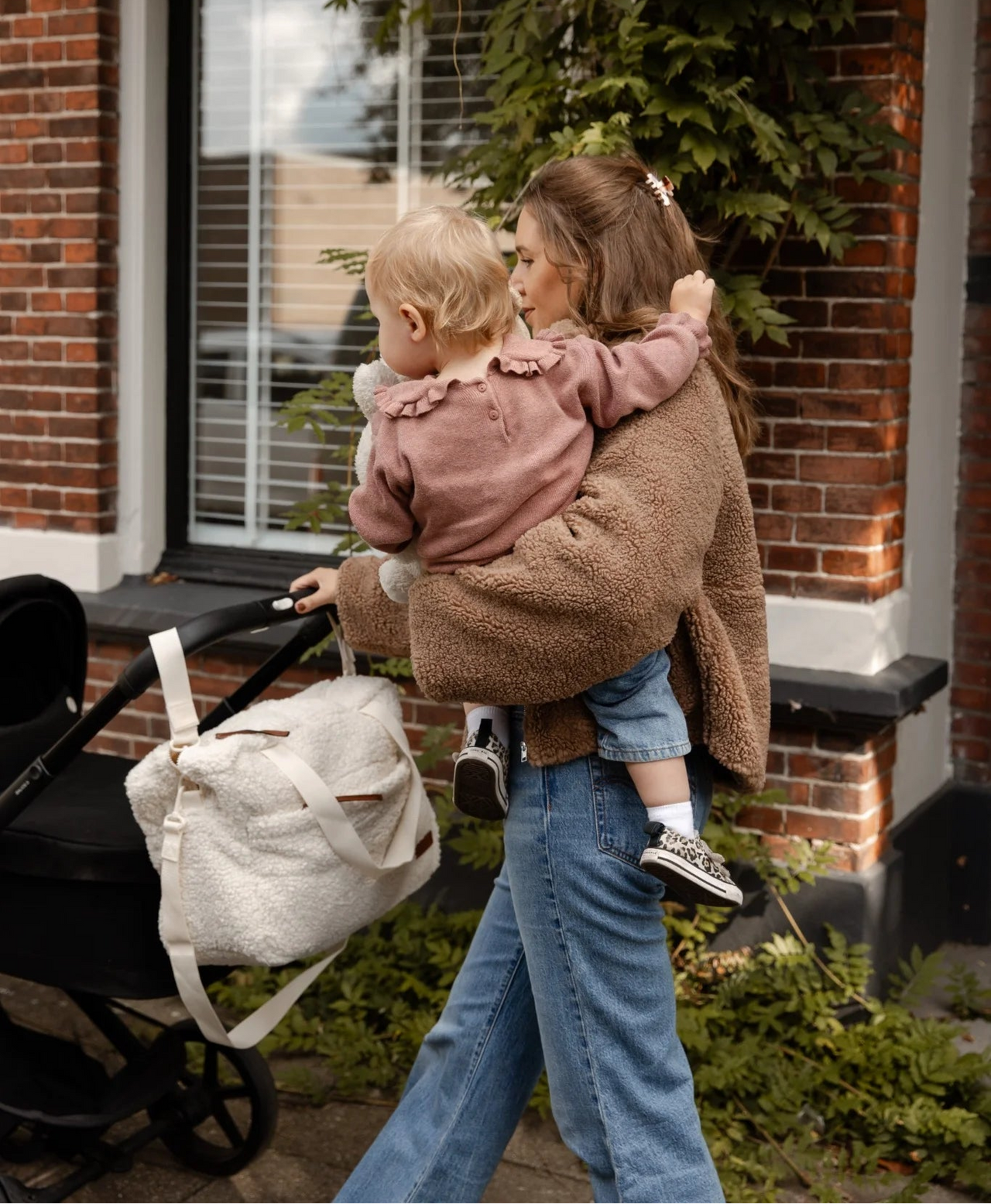 Moeder met kind en teddy luiertas cream van Benni & Ninni aan kinderwagen