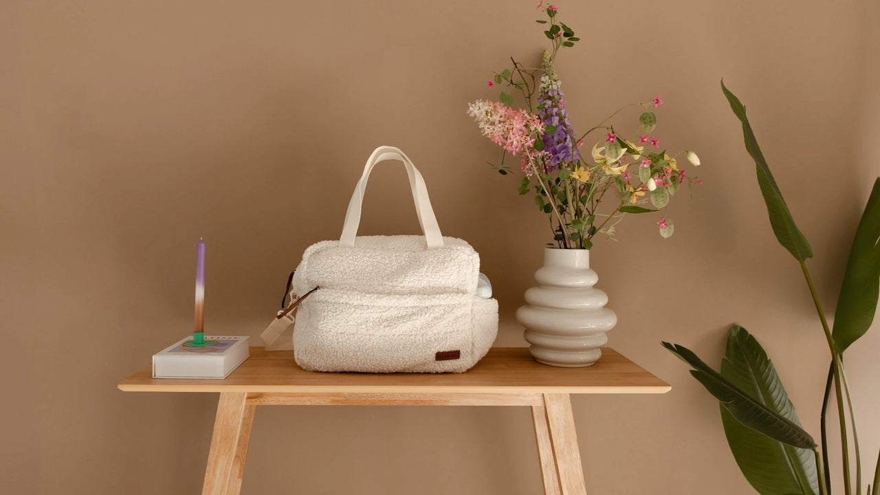 Teddy luiertas cream op houten tafel naast vaas met bloemen en kaars