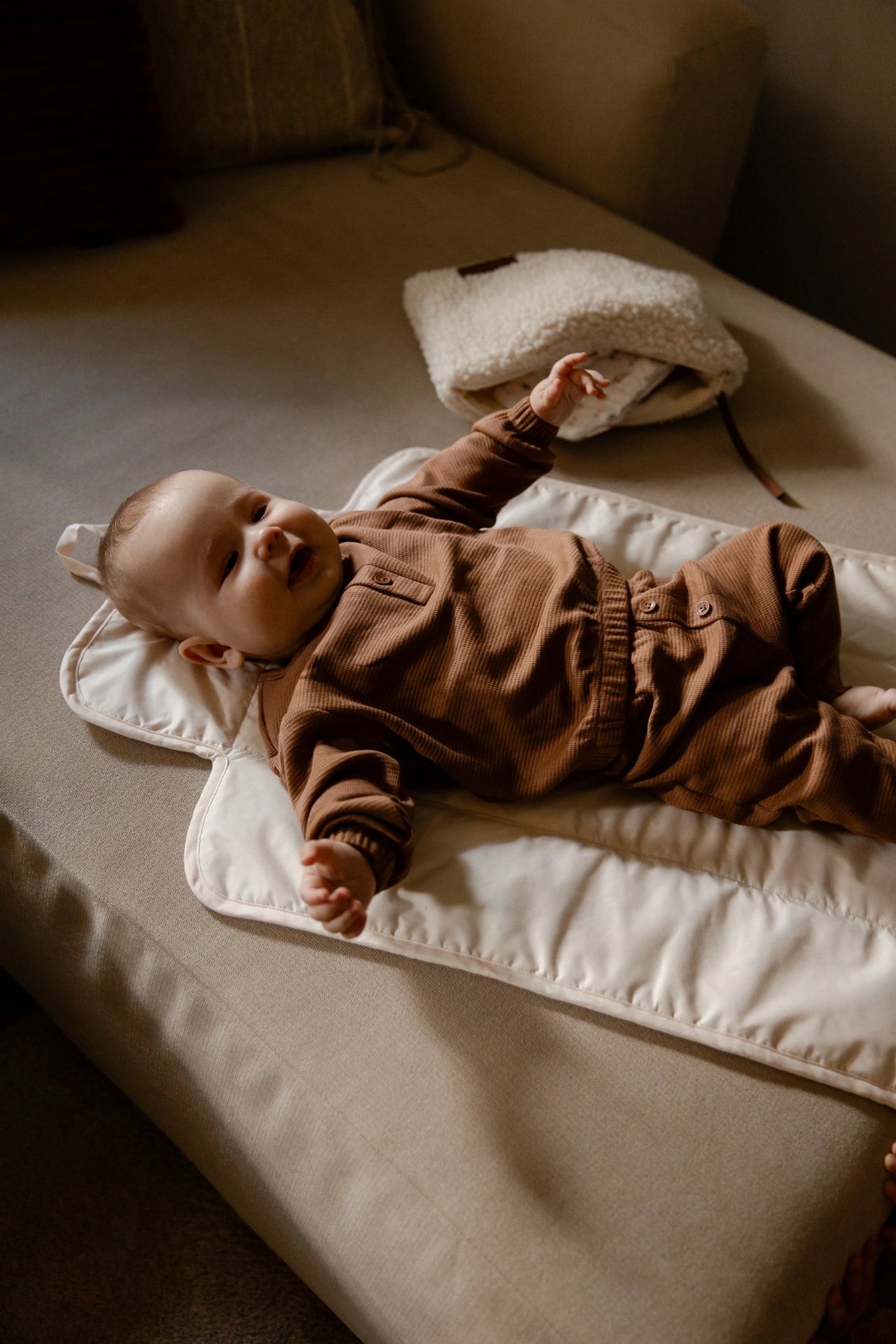 Baby ligt lachend op teddy verschoonmat cream